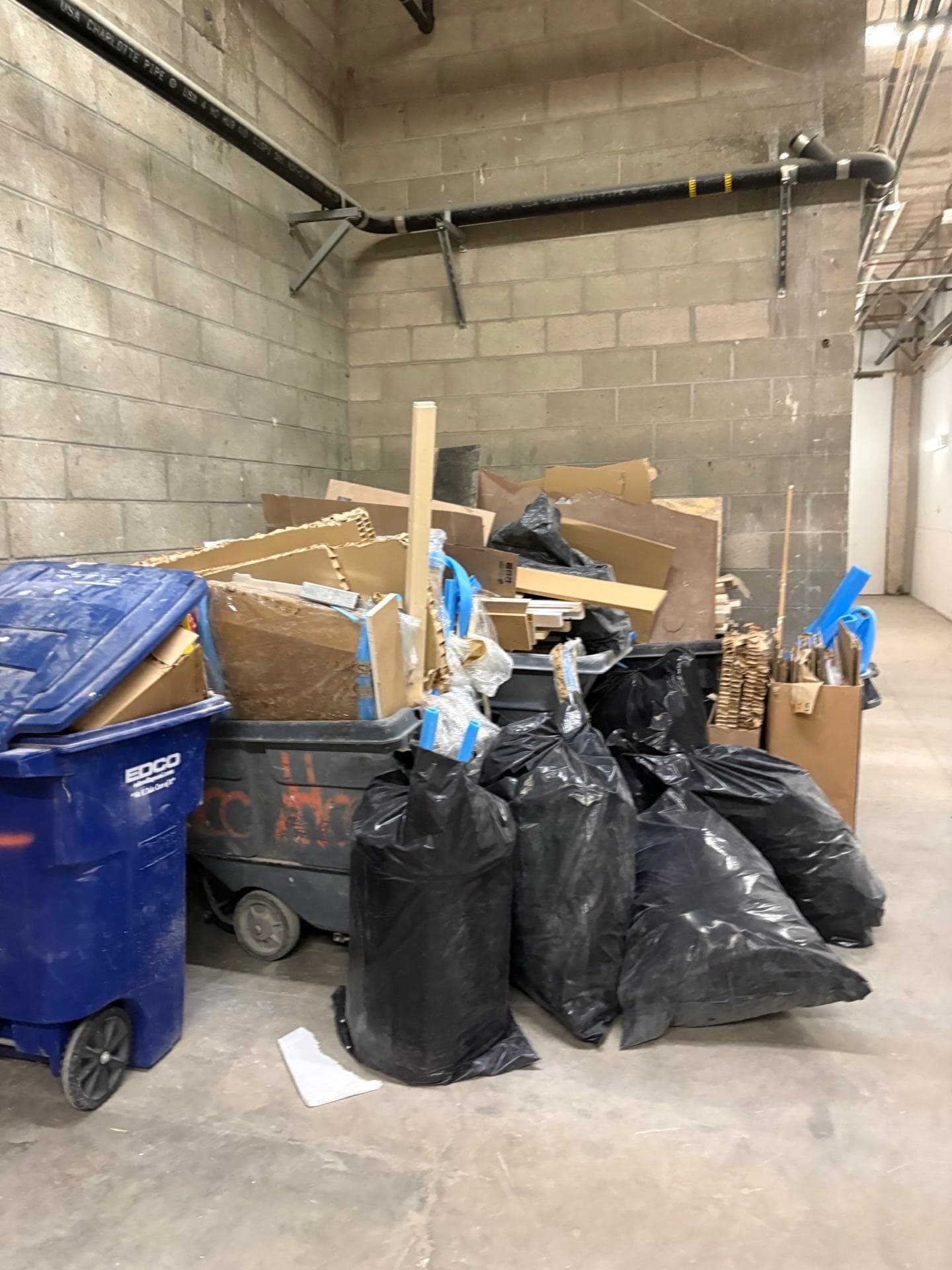 Construction debris pile — cardboard, trash bags, and lumber staged for JunkMD+ pickup in a San Diego loading dock