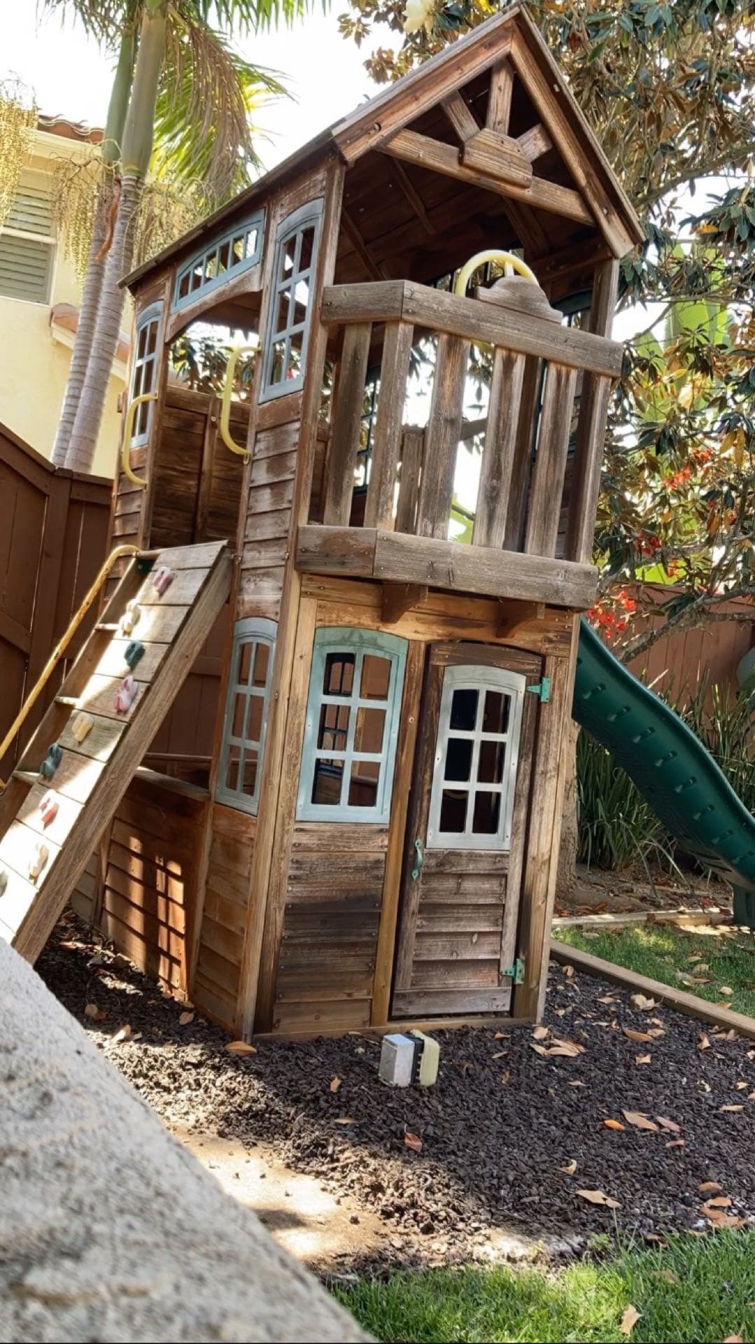 Wooden two-story backyard playhouse with green slide ready for JunkMD+ playset removal in San Diego