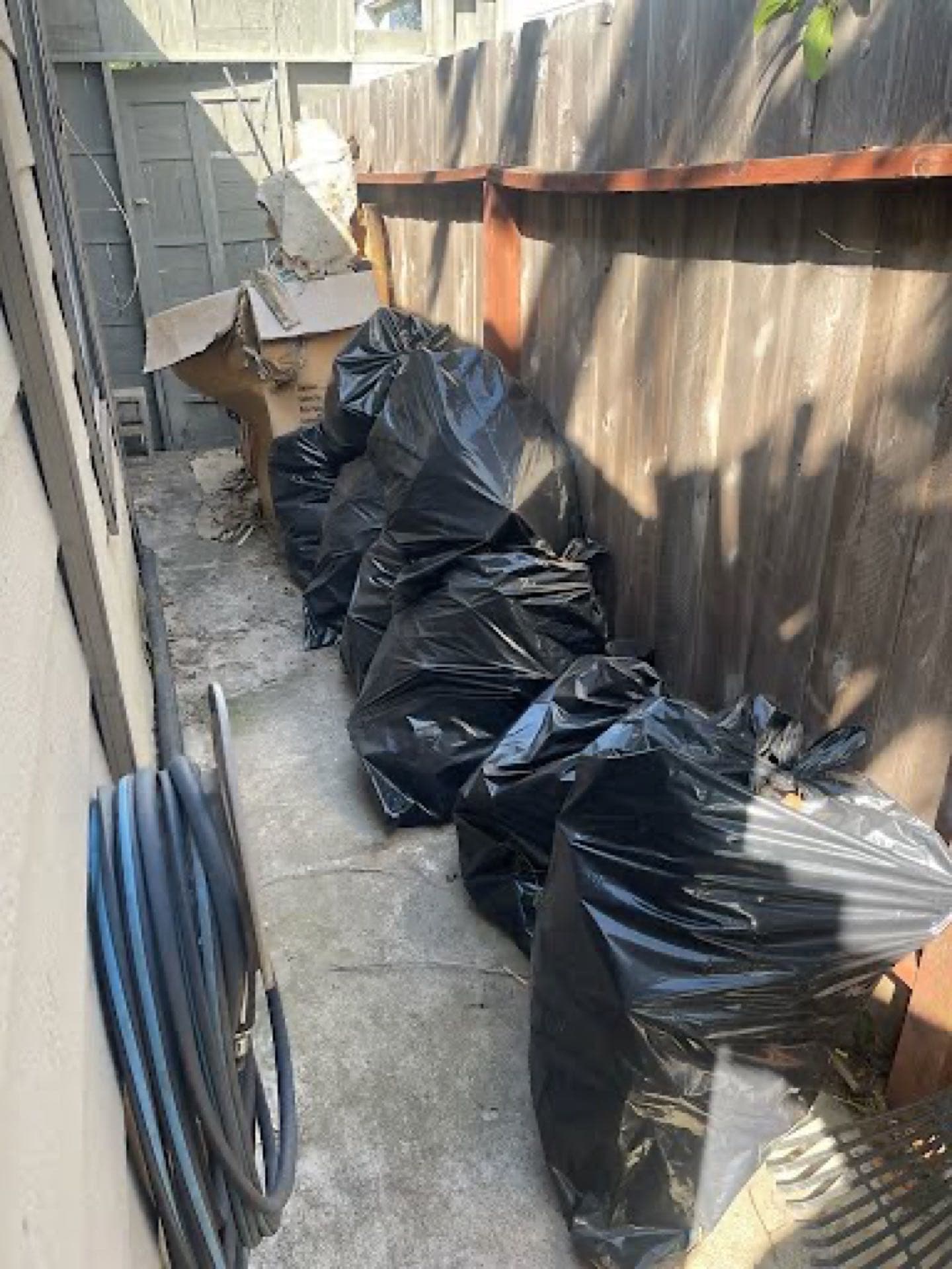 Trash bags of yard waste lined against a fence after a JunkMD+ San Diego cleanup