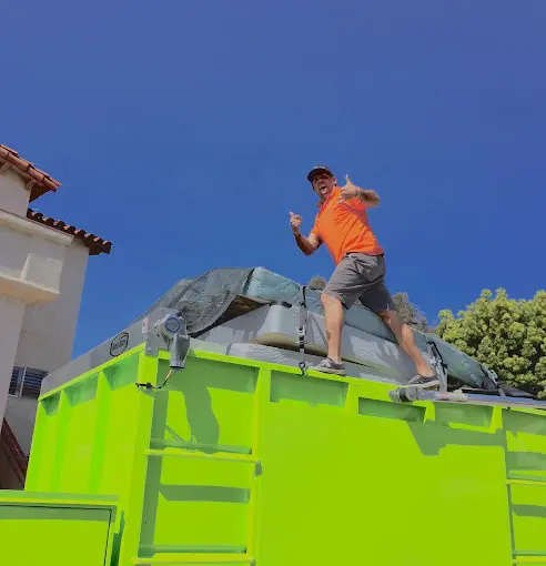 a man standing on top of a green dumpster