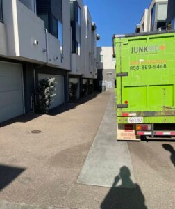 Green Junk MD removal truck parked in a narrow residential alleyway of modern townhouses for a junk removal project.