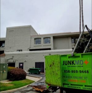 Green Junk MD junk removal and hauling truck parked at a large commercial building or apartment complex for professional debris removal.